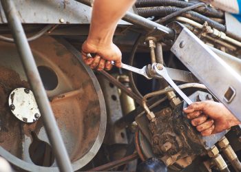 Combine machine service, mechanic repairing motor outdoors.